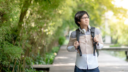Confident Asian man university student with glasses and headphones smiling and holding backpack in...