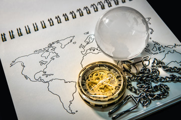 Gold pocket watch and world globe crystal glass on world map outline sketch on paper page of notebook. Travel around the world. Global business concept