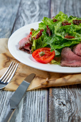 Salad leaves with sliced roast beef and sun-dried cherry tomatoes on wooden background