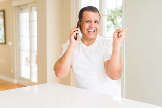Middle age man calling using smartphone very happy pointing with hand and finger to the side