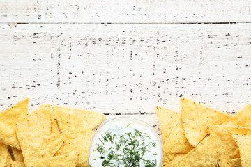 Potato chips with sauce and green dill on white wooden table