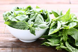 Green basil leafs in bowl on brown wooden table