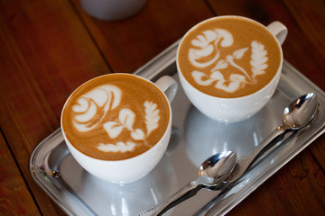Two white cups of cappuccino with rose pattern. Latte art coffee
