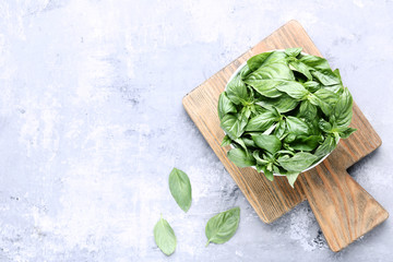 Green basil leafs in bowl with cutting board on grey wooden table