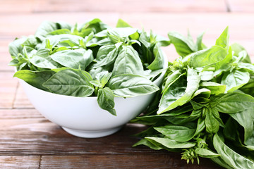 Green basil leafs in bowl on brown wooden table