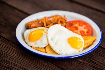 Typial breakfast with eggs, tomato, onion rings and sausage on plate