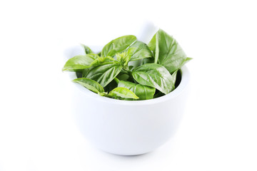 Green basil leafs in mortar isolated on white background