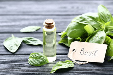 Bottle of essential oil with basil leafs and paper card on black wooden table