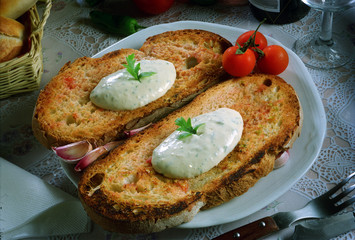 Dos rebanadas de pan tostado con tomate y ajo, y queso para untar.