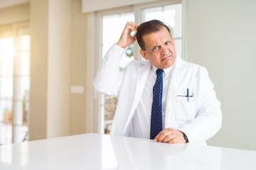 Fototapeta premium Middle age doctor man wearing medical coat at the clinic confuse and wonder about question. Uncertain with doubt, thinking with hand on head. Pensive concept.