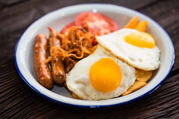 Typial breakfast with eggs, tomato, onion rings and sausage on plate