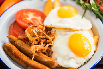 Typial breakfast with eggs, tomato, onion rings and sausage on plate