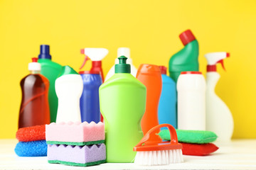 Bottles with detergent and cleaning tools on yellow background