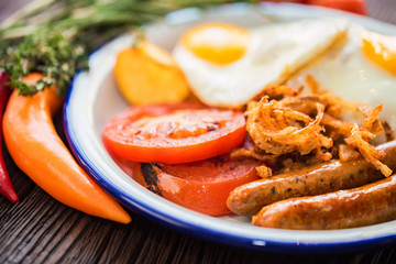 Typial breakfast with eggs, tomato, onion rings and sausage on plate