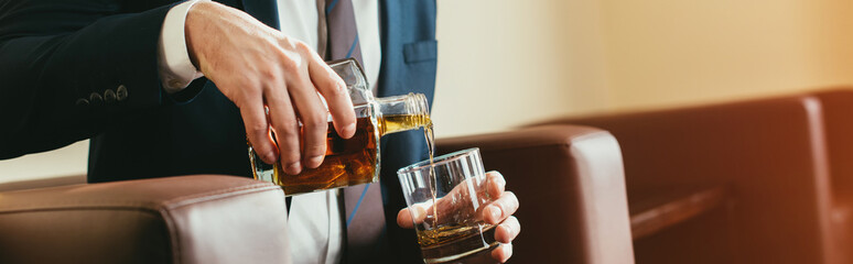 cropped view of businessman pouring whiskey from bottle into glass in hotel room