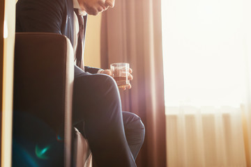 cropped view of upset businessman in formal wear holding glass of whiskey in hotel room