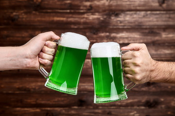 St. Patrick's Day. Glass mugs with green beer in male hands on wooden background
