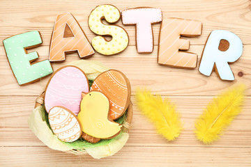 Gingerbread cookies with word Easter and yellow feathers on wooden table