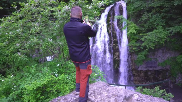 Man admiring the waterfall and doing photos on smartphone