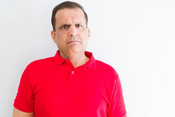 Middle age man wearing red t-shirt over white wall with serious expression on face. Simple and natural looking at the camera.
