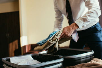 cropped view of businessman putting clothes into travel bag