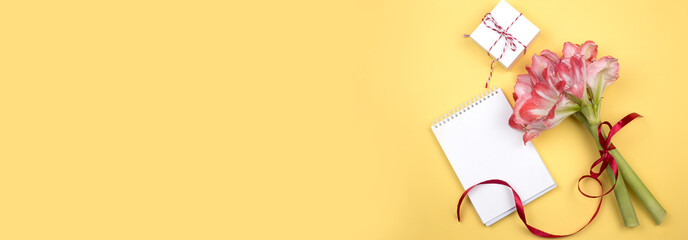 Open blank notepad and bouquet of pink  flowers on yellow background top view in flat lay style.