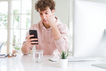 Young student man using smartphone and computer annoyed and frustrated shouting with anger, crazy and yelling with raised hand, anger concept