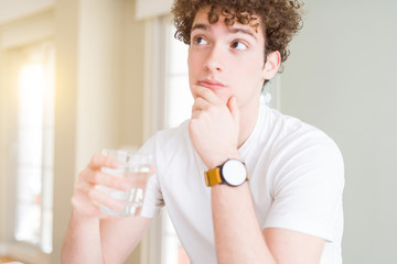 Young man drinking a glass of water at home serious face thinking about question, very confused idea