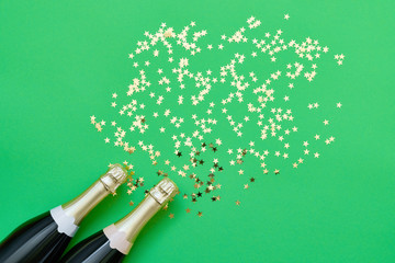 Two champagne bottle with confetti stars on green background.  Copy space, top view