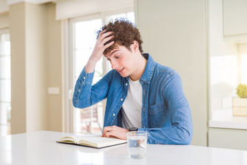 Fototapeta premium Young man reading a book at home stressed with hand on head, shocked with shame and surprise face, angry and frustrated. Fear and upset for mistake.
