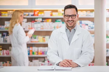 Ingelijste posters Portrait of a handsome pharmacist at the counter of a drugstore, female colleague working in the background. © bnenin