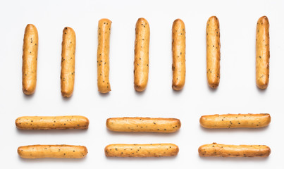 Crispy breadsticks with poppy seeds arranged in rows on a white background