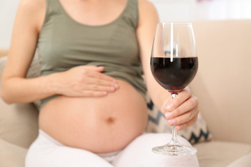 Pregnant woman with glass of red wine at home, space for text. Alcohol addiction
