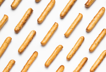 Crispy breadsticks with poppy seeds arranged in rows on a white background