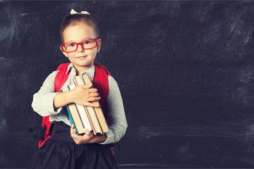 Cute little schoolgirl in glasses on blackboard background