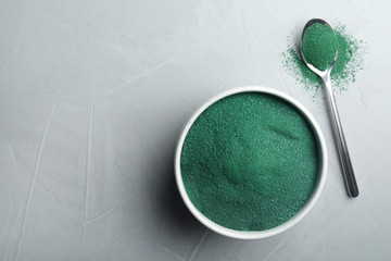 Bowl and spoon of spirulina algae powder on grey background, top view with space for text
