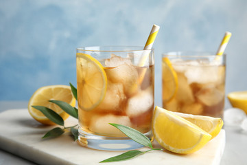 Glasses of lemonade with ice cubes and fruit on table against color background