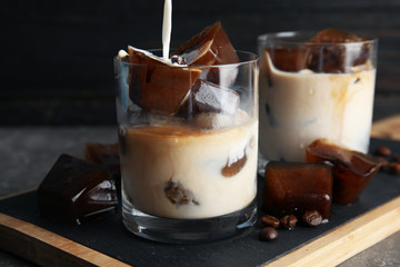 Pouring milk into glass with coffee ice cubes on table