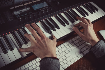 Male musician playing midi keyboard synthesizer in recording studio, focus on hands. Close-up