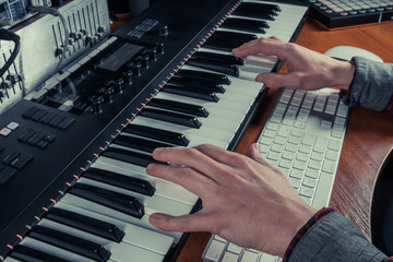 Fototapeta na wymiar Male musician playing midi keyboard synthesizer in recording studio, focus on hands. Close-up