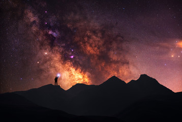 A beautiful starry night, a silhouette of a man, stands on a mountain and looks at the Milky Way...