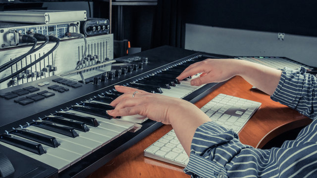 Female musician playing midi keyboard synthesizer in recording studio, focus on hands. Womans arms plays solo of music or new melody.
