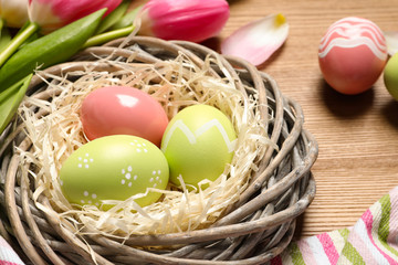 Wicker nest with painted Easter eggs on wooden table