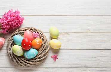 Fototapeta na wymiar Flat lay composition of wicker nest with colorful painted Easter eggs and flower on table, space for text