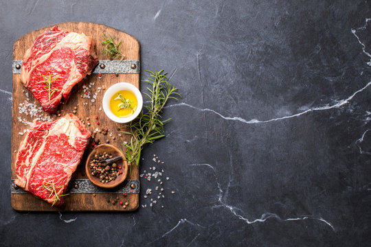 Raw Fresh Marbled Meat Beef Steak rosemary, spices  and vintage ax  on a wooden board. Black marble background. Top View Copy space for Text