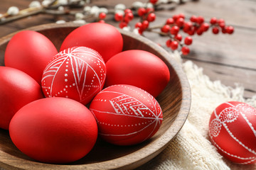 Wooden bowl with red painted Easter eggs on table, closeup
