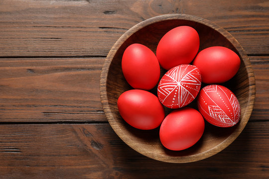 Wooden bowl with painted red Easter eggs on table, top view. Space for text