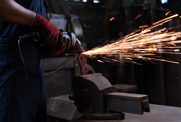 mechanical engineer technician operating an angle grinder power tool on metal clamped to a workshop...