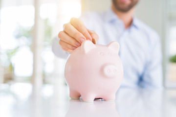 Close up of man hand putting a coin inside of piggy bank as savings