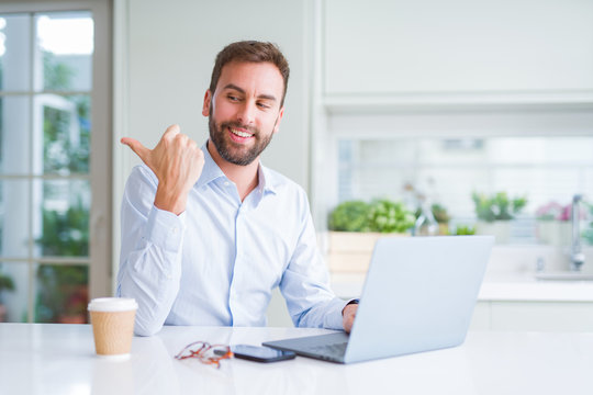Handsome man working using computer laptop and drinking a cup of coffee pointing and showing with thumb up to the side with happy face smiling